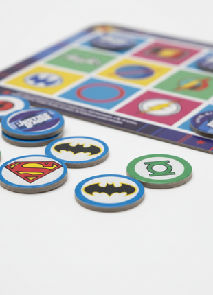 Justice League Bingo detalle fichas con escudos DC - Superman, Batman, Flash, colores vivos y acabado premium